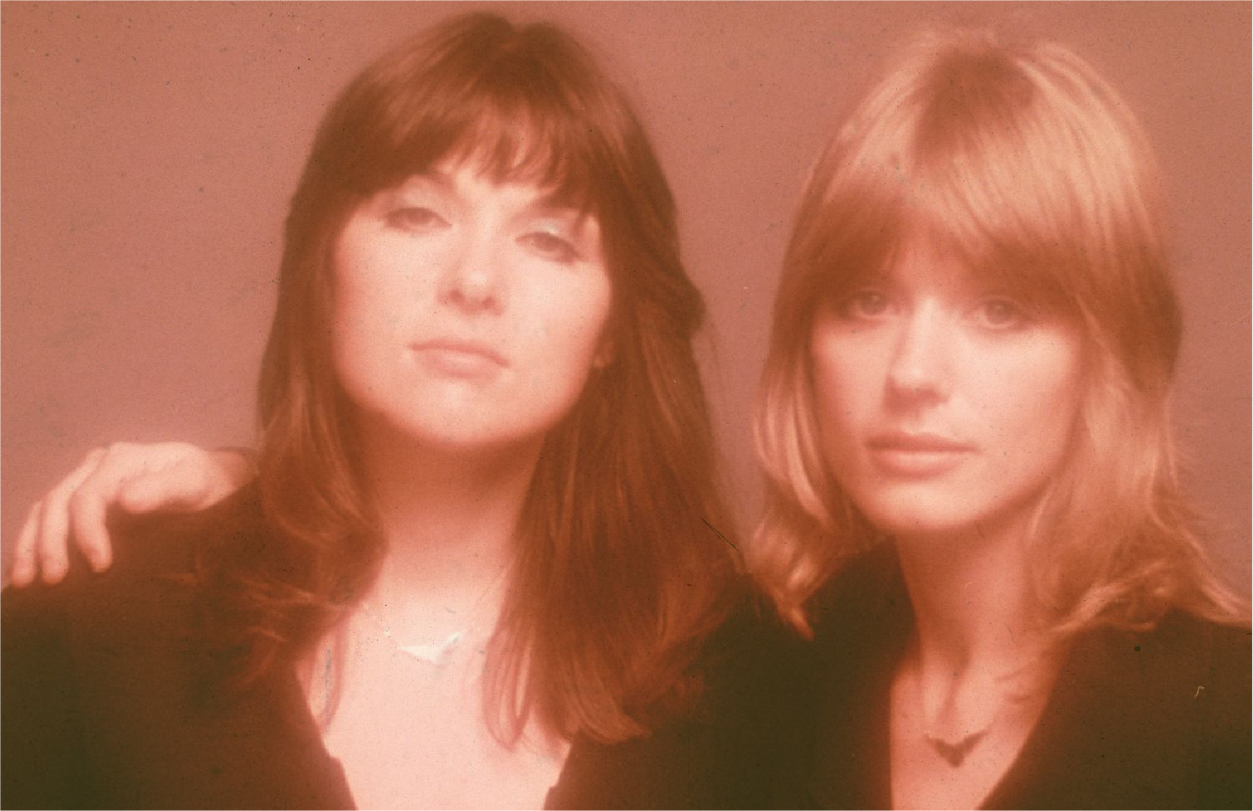 warm-toned dewy bust photo of Ann and Nancy Wilson, with Nancy's arm on Ann's shoulder